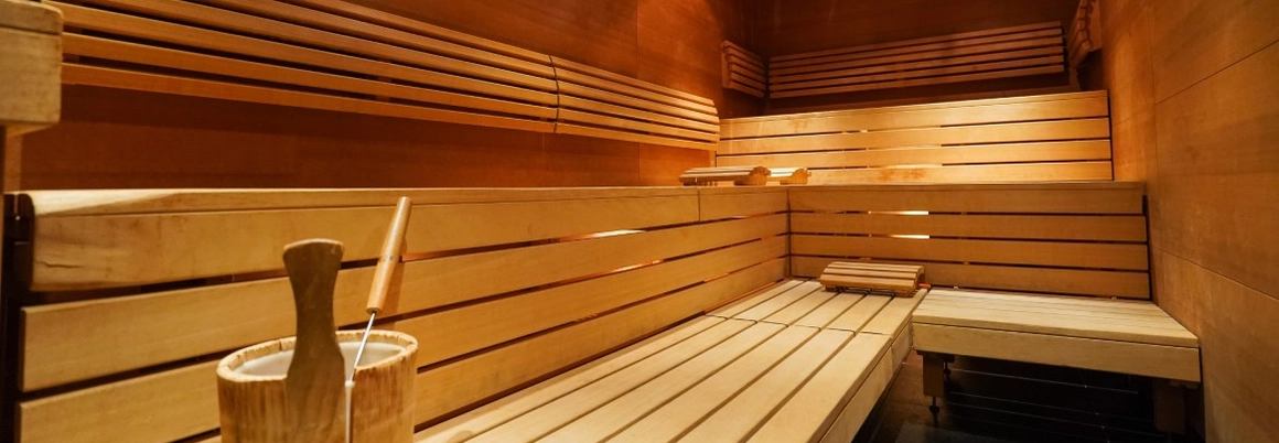 Innenansicht einer leeren Holzsauna mit Aufgusseimer und Kelle.